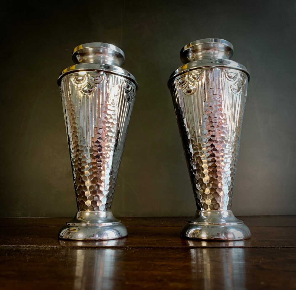 A pair of Art Deco chrome-plated metal vases with hammered lower bodies, geometric moulding near the rim, and circular stepped bases.