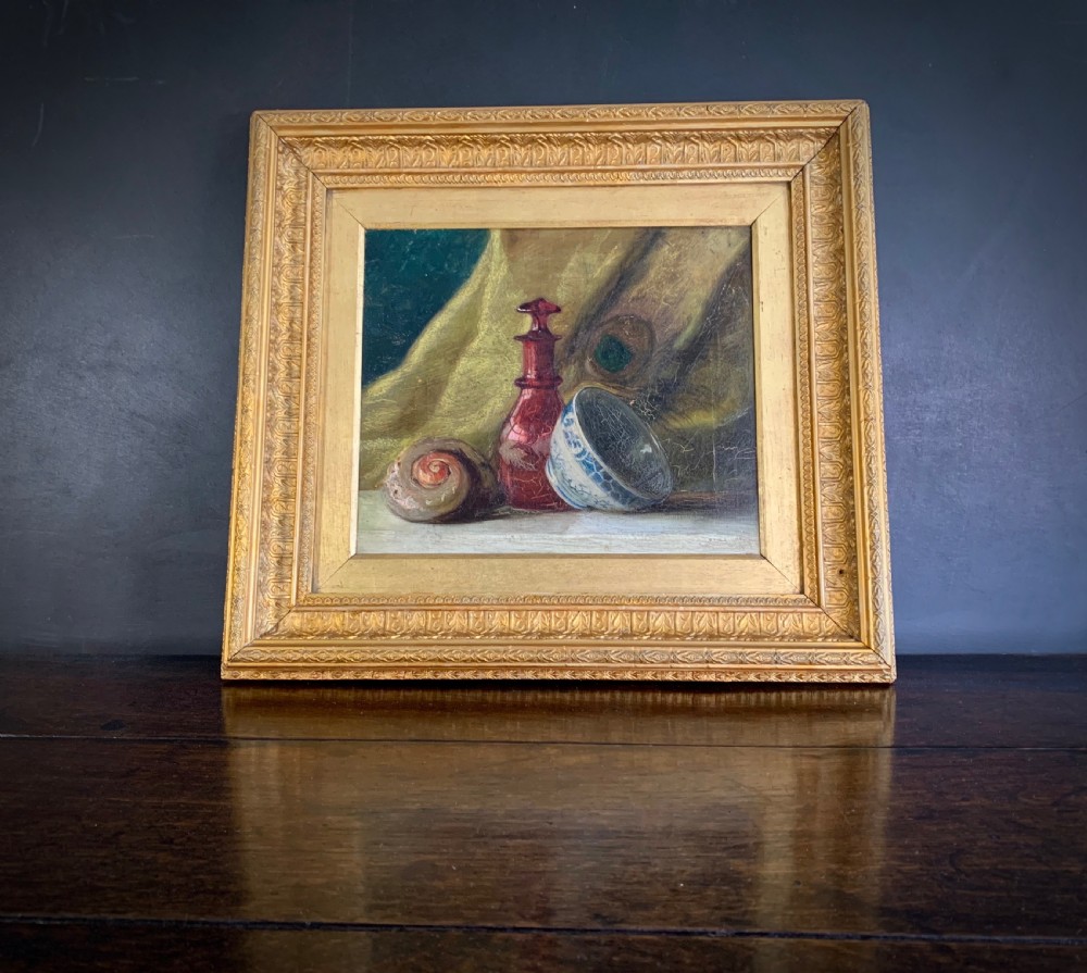 A 19th-century framed oil painting depicting a seashell, a red glass bottle, and a porcelain bowl set against draped fabric.