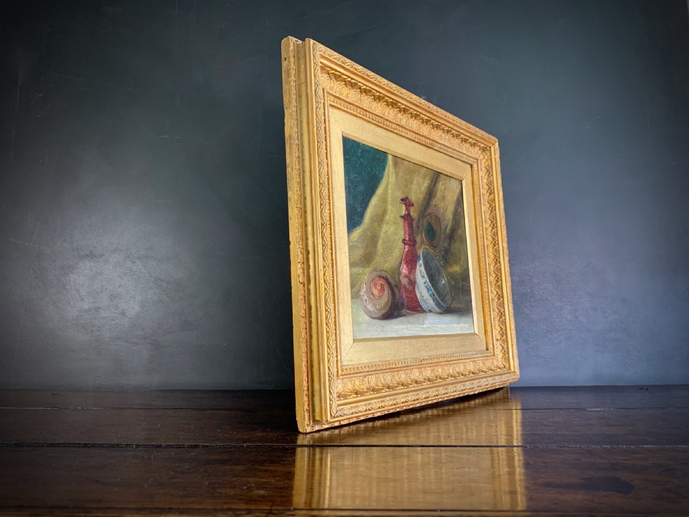 A 19th-century framed oil painting depicting a seashell, a red glass bottle, and a porcelain bowl set against draped fabric. View XII