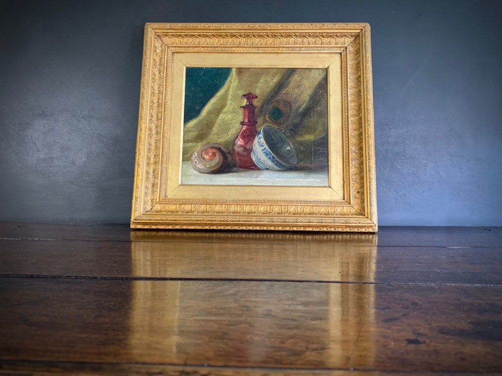 A 19th-century framed oil painting depicting a seashell, a red glass bottle, and a porcelain bowl set against draped fabric. View XIV