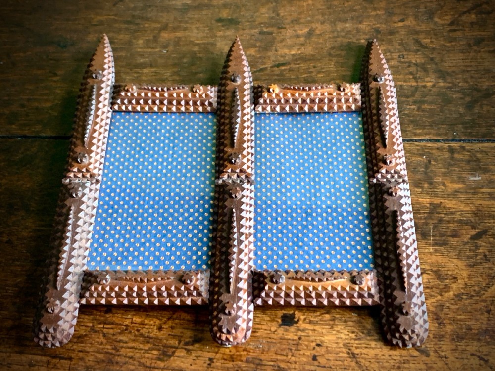 An antique tramp art double picture frame made of carved wood with layered notched geometric borders.