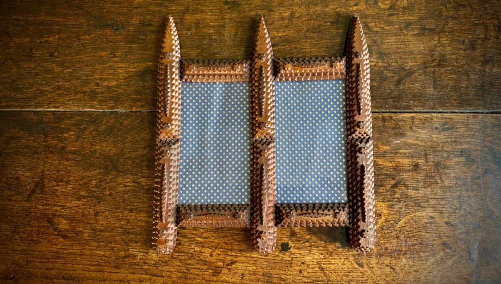 An antique tramp art double picture frame made of carved wood with layered notched geometric borders. View II