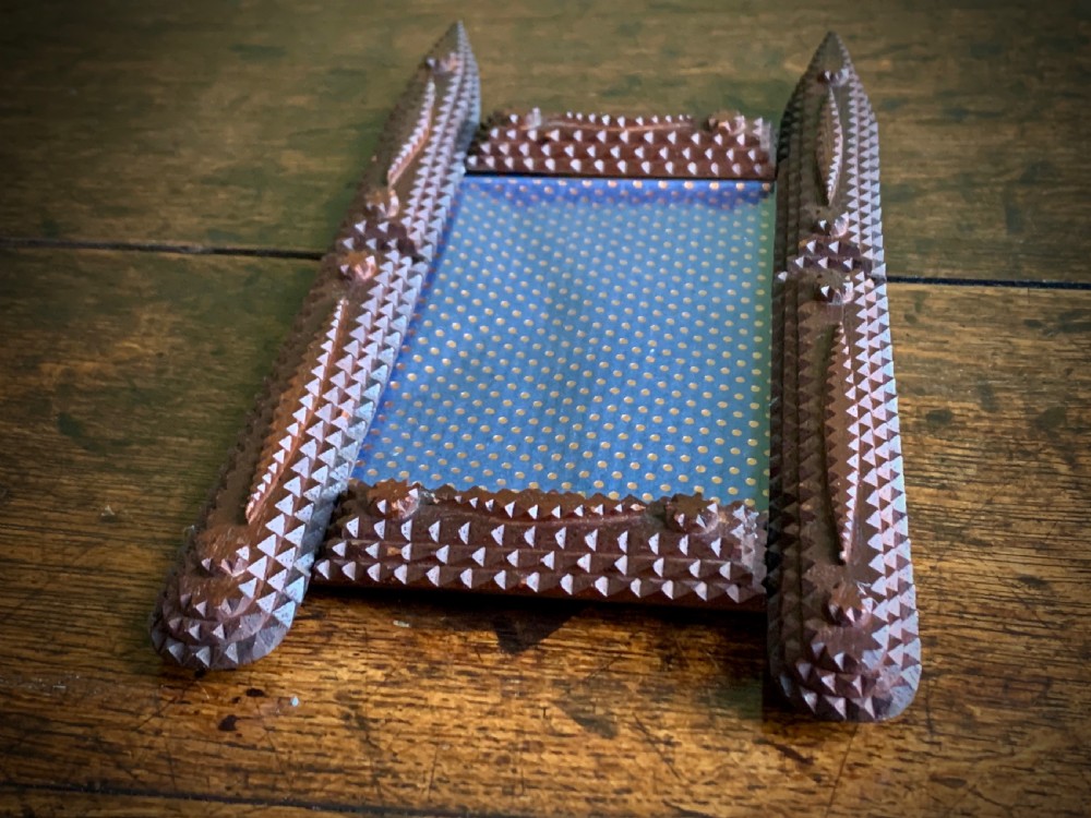 A dark brown hand-carved tramp art wooden picture frame featuring notch-carved geometric borders and pointed finials encasing a monochrome portrait photograph. View IV