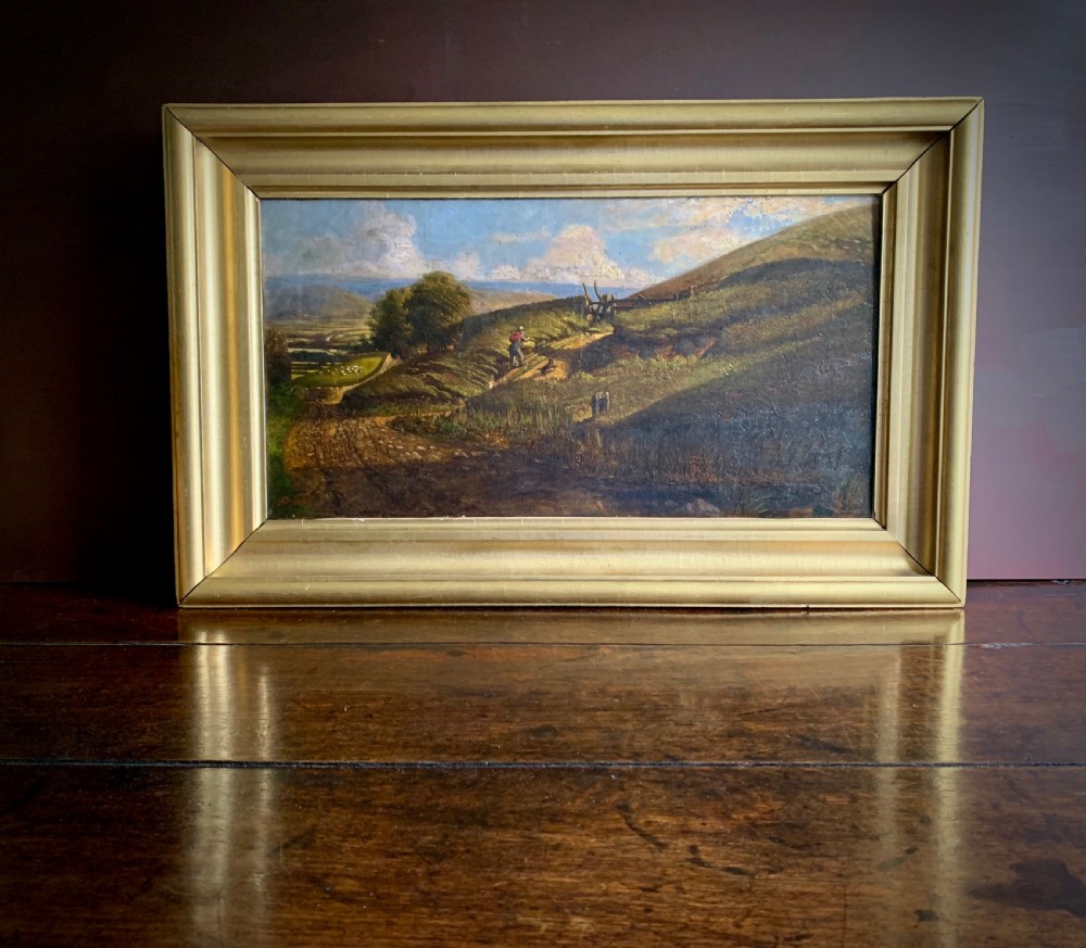 A nineteenth-century framed landscape oil painting depicting a figure walking along a sunlit green hillside.