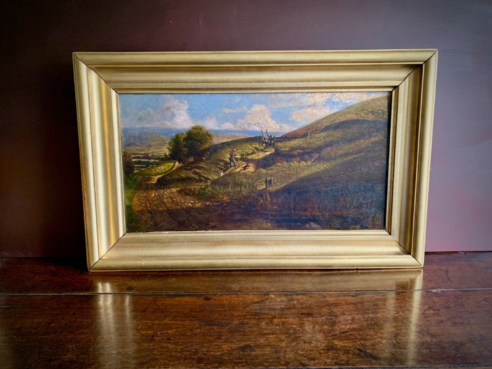 A nineteenth-century framed landscape oil painting depicting a figure walking along a sunlit green hillside. View IX