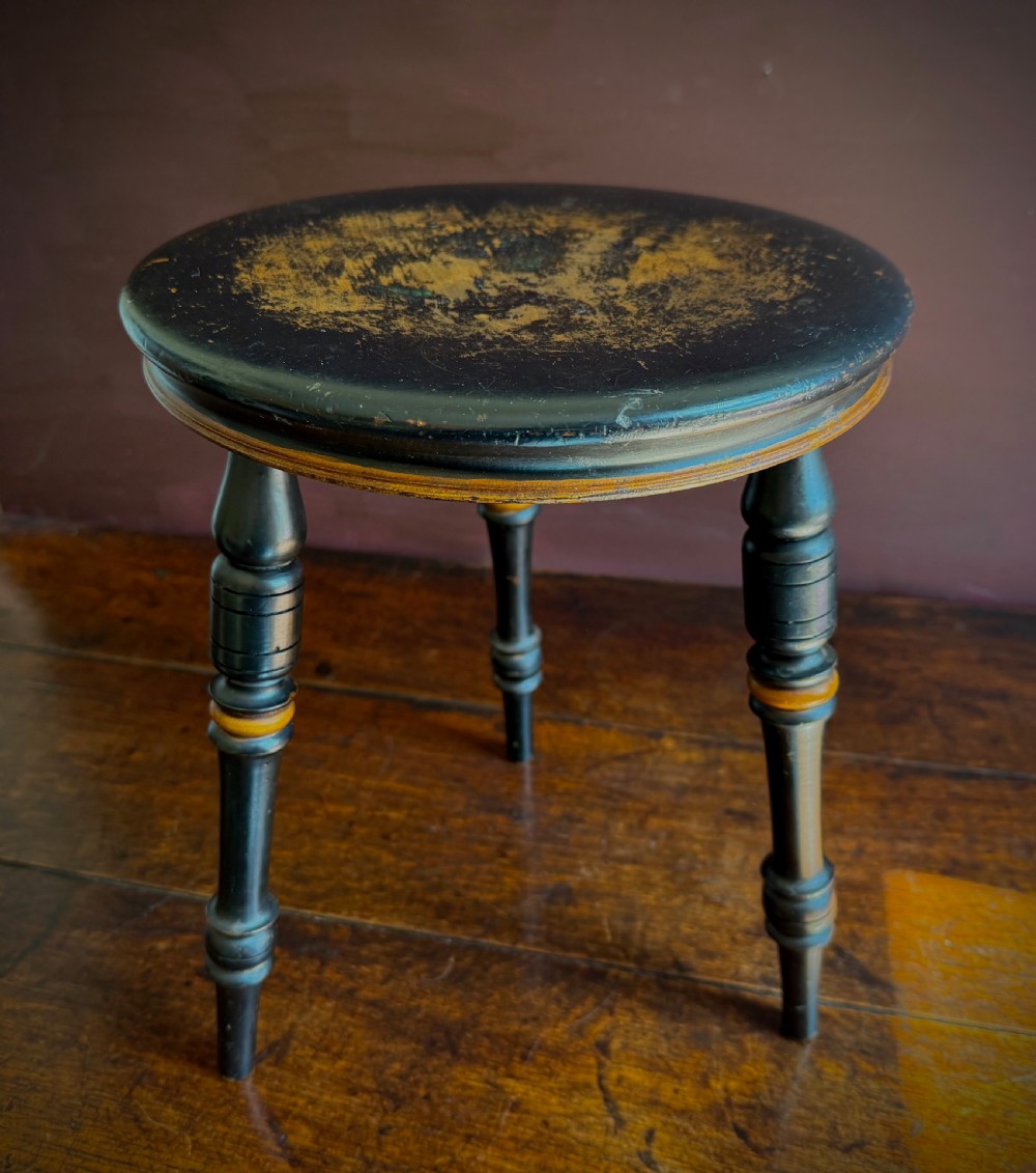 A Victorian ebonised three-legged stool featuring turned legs with gilt band highlights and a circular top showing surface wear. View III