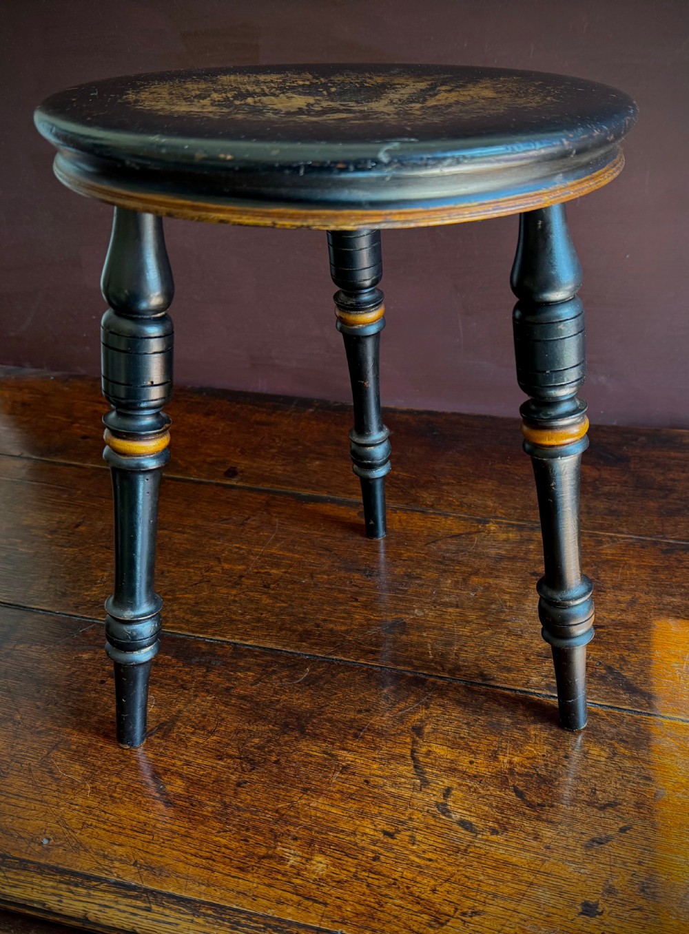 A Victorian ebonised three-legged stool featuring turned legs with gilt band highlights and a circular top showing surface wear. View VII
