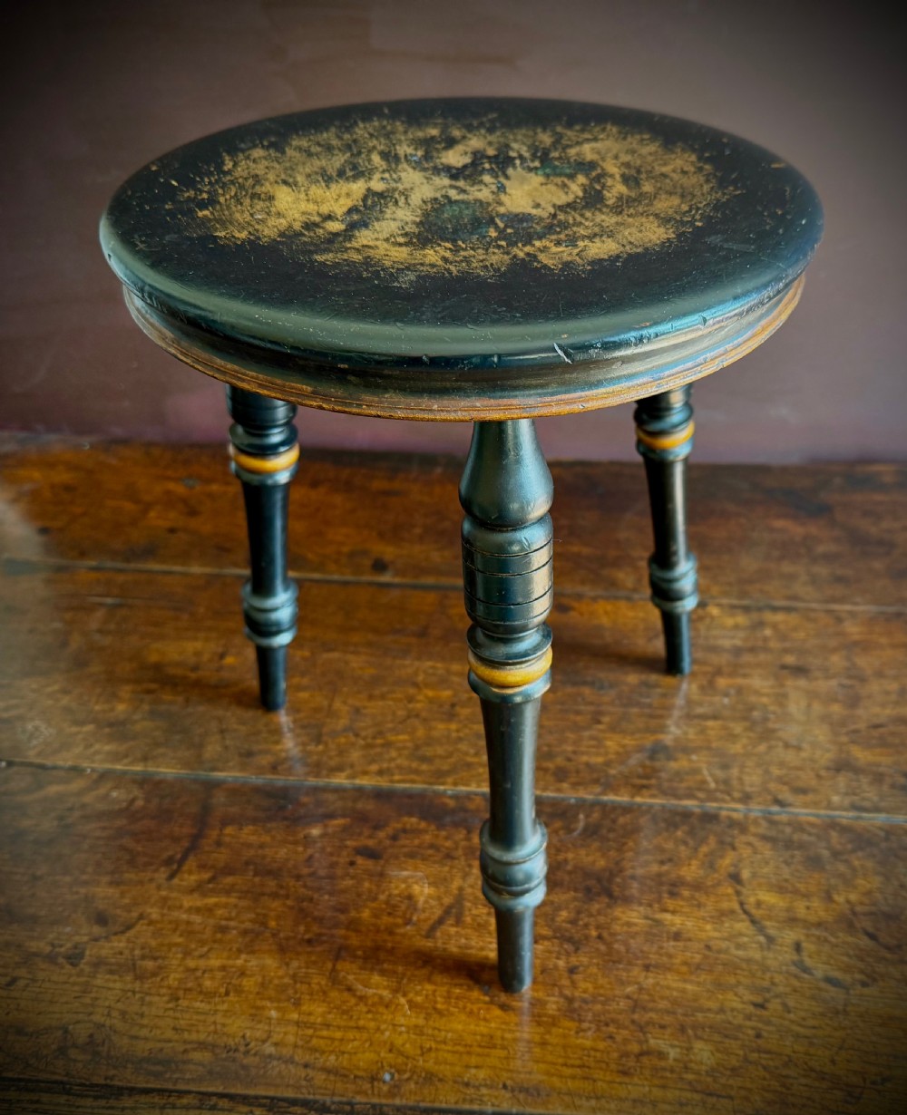 A Victorian ebonised three-legged stool featuring turned legs with gilt band highlights and a circular top showing surface wear. View XI