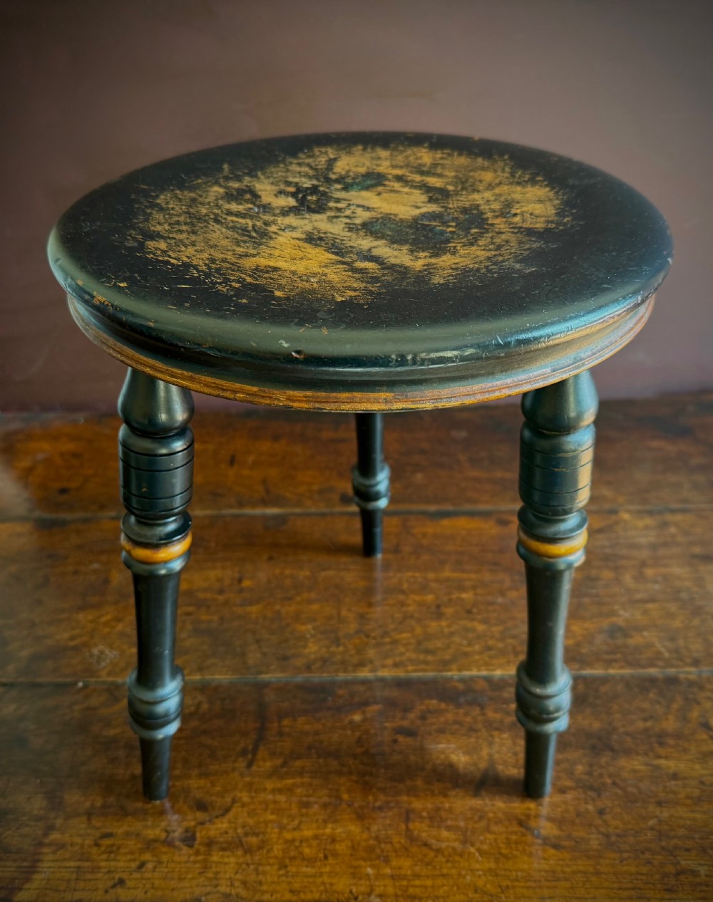 A Victorian ebonised three-legged stool featuring turned legs with gilt band highlights and a circular top showing surface wear. View XII