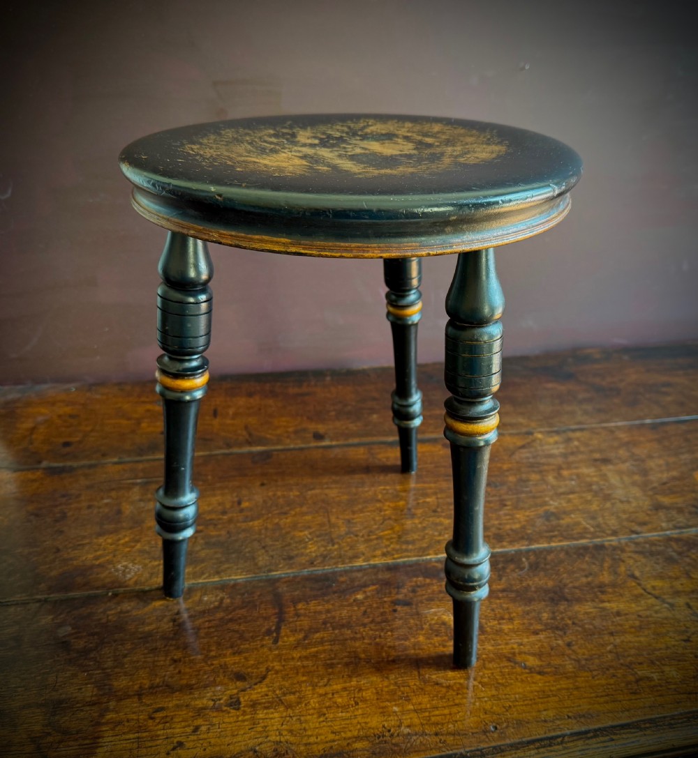 A Victorian ebonised three-legged stool featuring turned legs with gilt band highlights and a circular top showing surface wear. View XIII