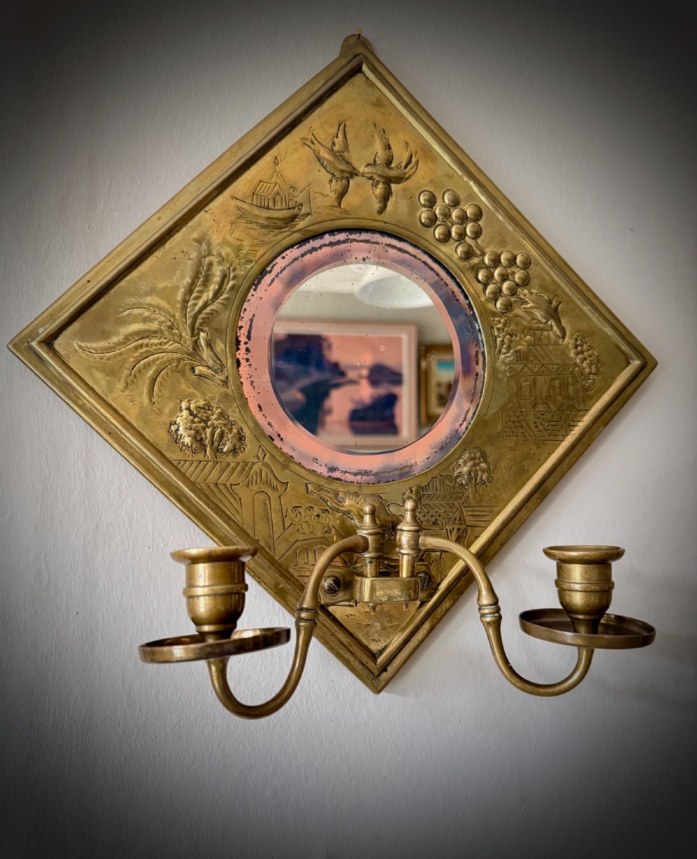 A pair of diamond-shaped embossed brass girandole wall mirrors featuring Chinoiserie scenes and twin candle branches. View V