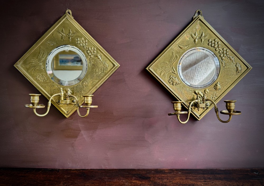 A pair of diamond-shaped embossed brass girandole wall mirrors featuring Chinoiserie scenes and twin candle branches. View XVII