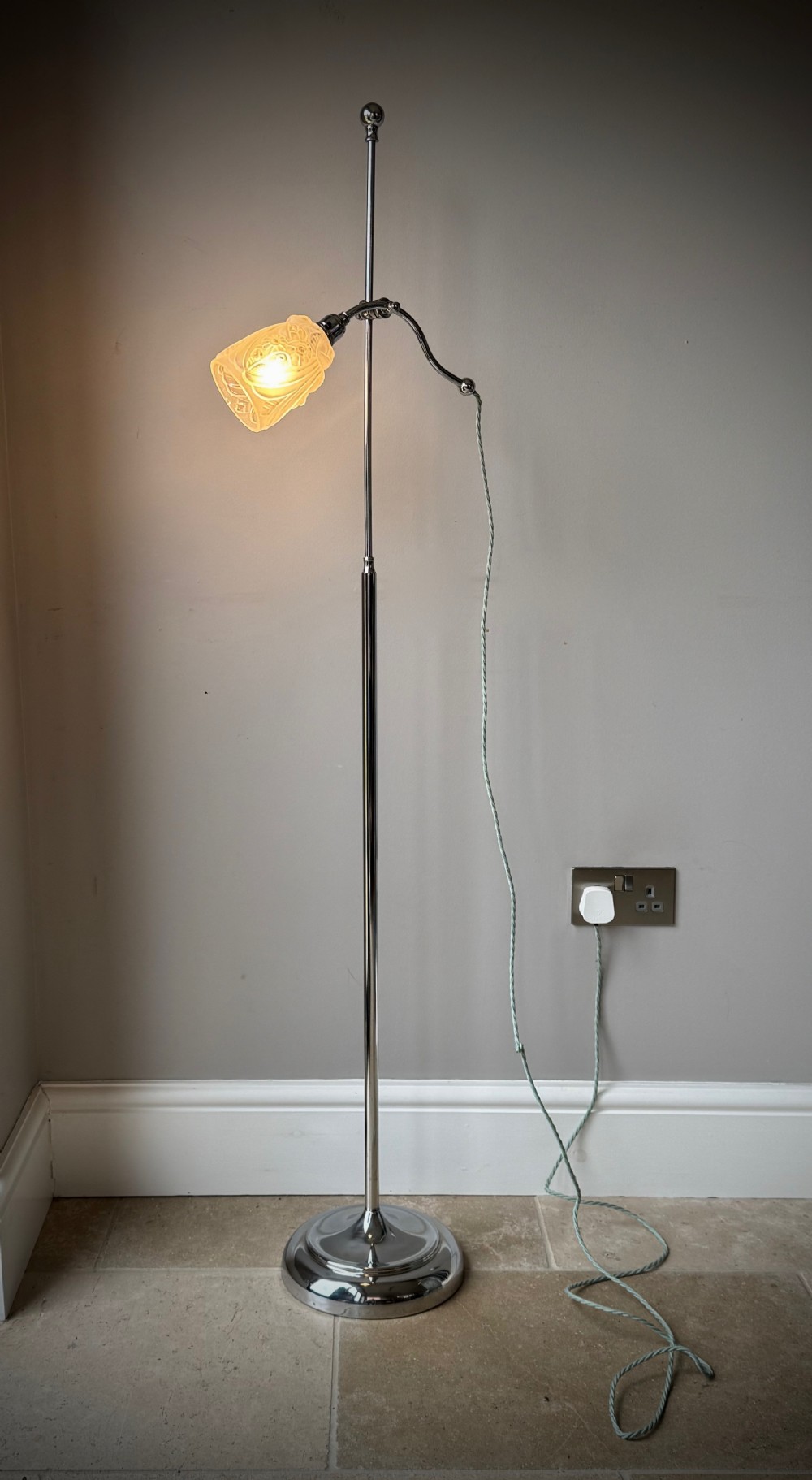 A slender 1920s Art Deco adjustable floor lamp crafted from polished chrome with an articulated neck and a lit frosted glass shade.