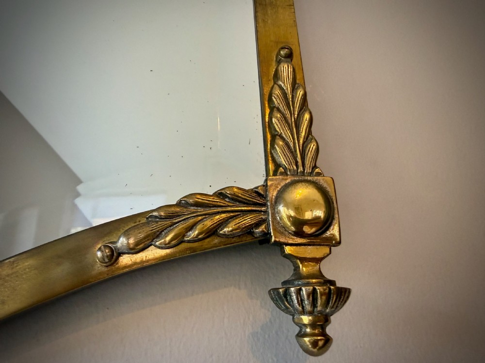 Horizontal wall mirror featuring a brass frame with sculpted rams heads on the top corners, leaf motifs, a curved lower edge, and an overhead hanging chain. View IX