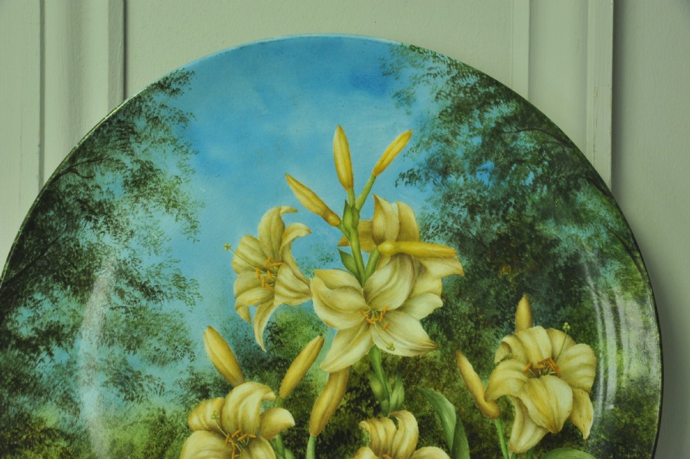 A circular hand-painted porcelain decorative plate displaying yellow lilies against foliage and a blue sky. View IV