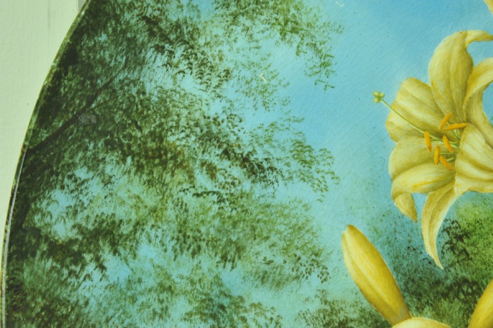 A circular hand-painted porcelain decorative plate displaying yellow lilies against foliage and a blue sky. View IX