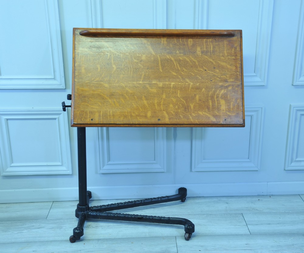 An antique adjustable oak top reading table mounted on a black cast iron pedestal base with castors.