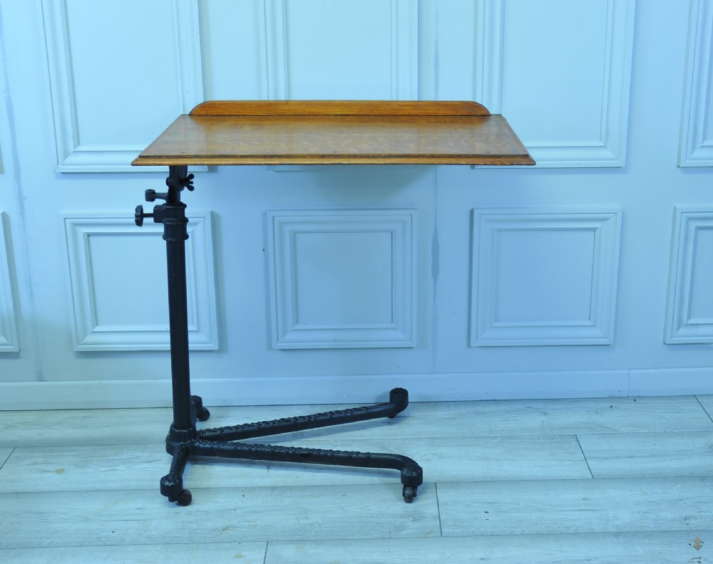 An antique adjustable oak top reading table mounted on a black cast iron pedestal base with castors. View III