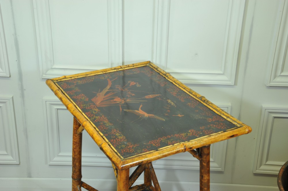 A late Victorian two-tier bamboo side table featuring a dark lacquered top panel decorated with botanical flora and birds. View V