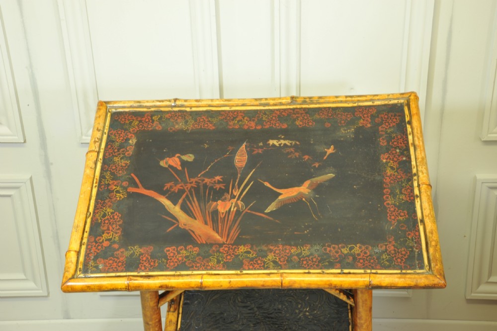 A late Victorian two-tier bamboo side table featuring a dark lacquered top panel decorated with botanical flora and birds. View X