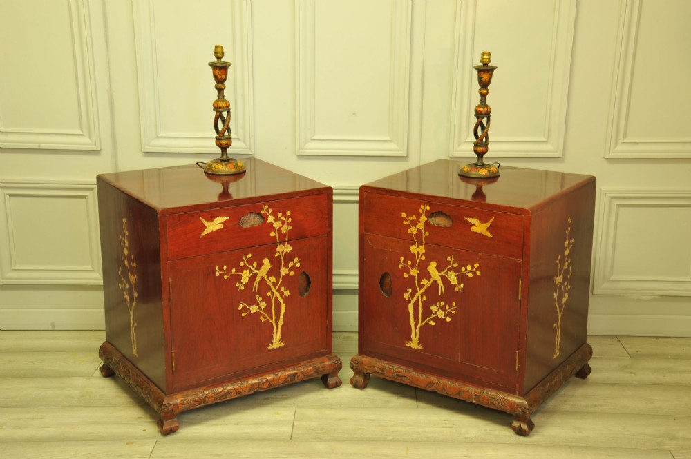 A pair of reddish-brown wood side cabinets featuring hand-painted gilt Chinoiserie floral and bird motifs resting on carved plinths.