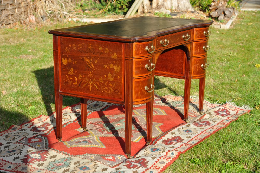 An antique Edwardian inlaid mahogany writing desk featuring a dark leather inset top, seven drawers with brass handles, and floral marquetry side panels. View II