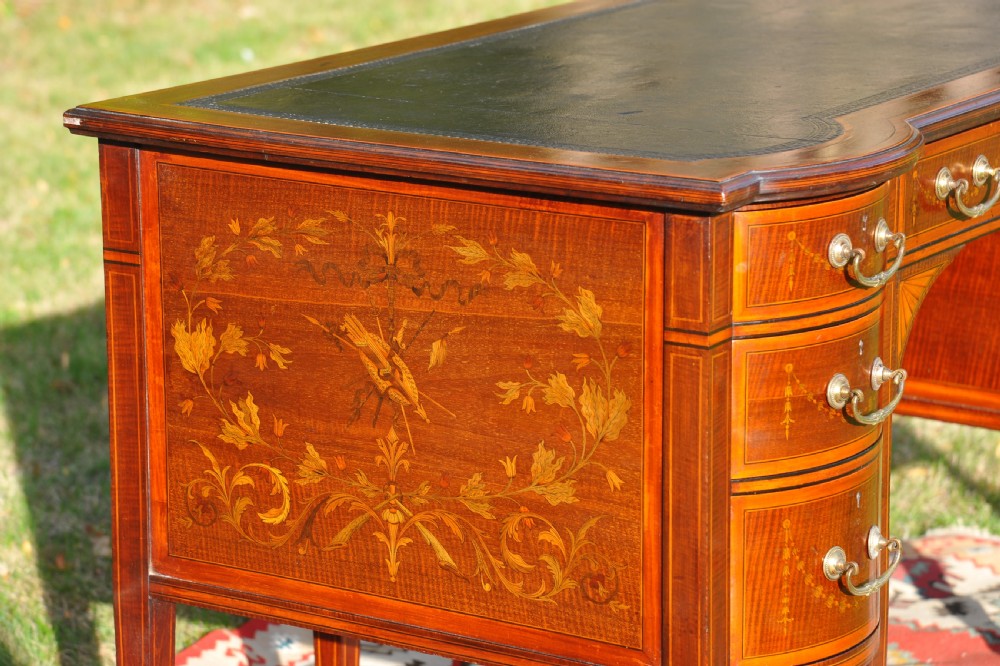 An antique Edwardian inlaid mahogany writing desk featuring a dark leather inset top, seven drawers with brass handles, and floral marquetry side panels. View III