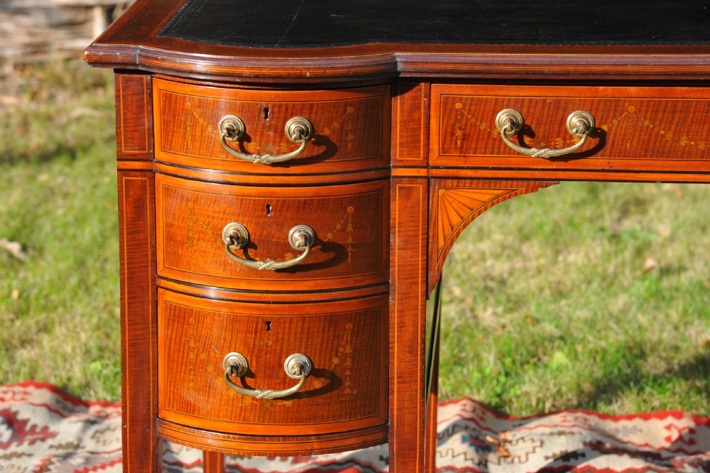 An antique Edwardian inlaid mahogany writing desk featuring a dark leather inset top, seven drawers with brass handles, and floral marquetry side panels. View VII