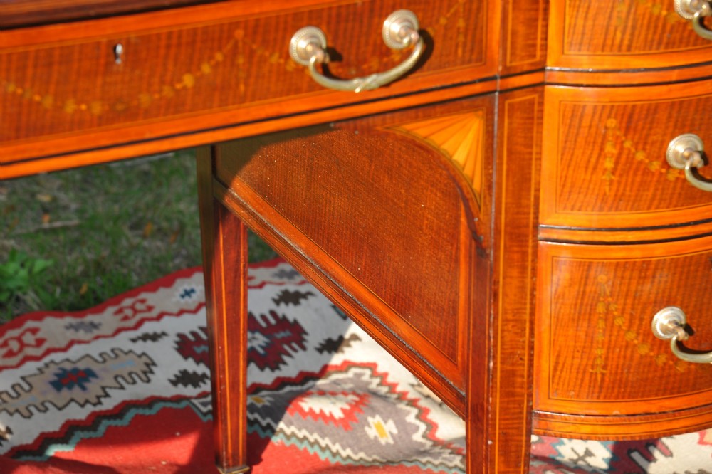 An antique Edwardian inlaid mahogany writing desk featuring a dark leather inset top, seven drawers with brass handles, and floral marquetry side panels. View VIII