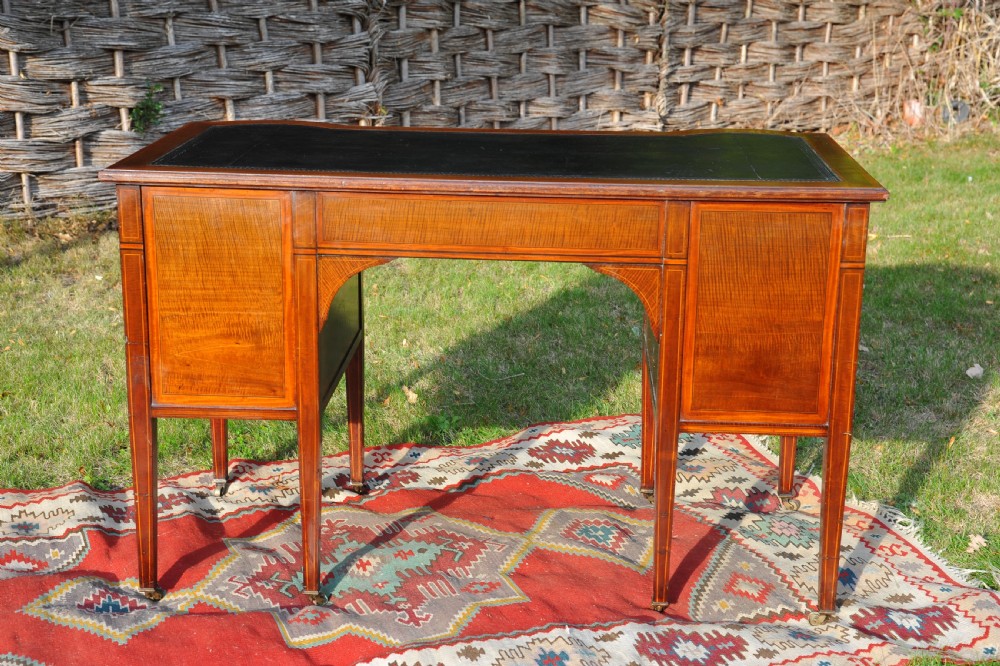 An antique Edwardian inlaid mahogany writing desk featuring a dark leather inset top, seven drawers with brass handles, and floral marquetry side panels. View XI