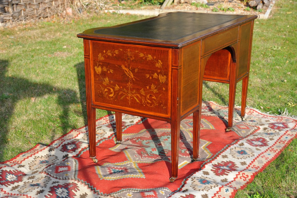 An antique Edwardian inlaid mahogany writing desk featuring a dark leather inset top, seven drawers with brass handles, and floral marquetry side panels. View XII