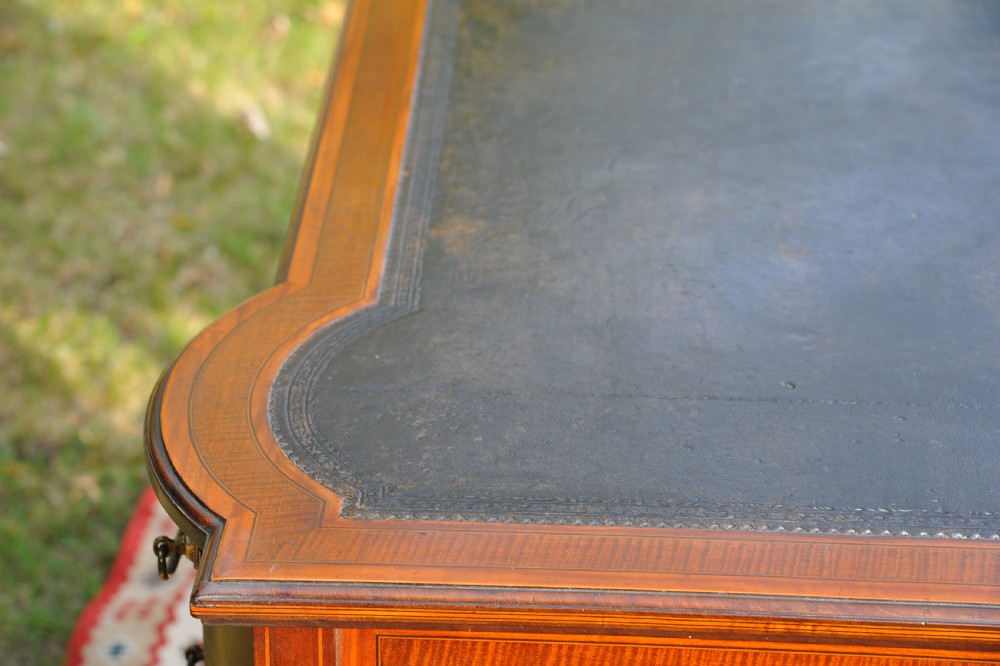 An antique Edwardian inlaid mahogany writing desk featuring a dark leather inset top, seven drawers with brass handles, and floral marquetry side panels. View XIV