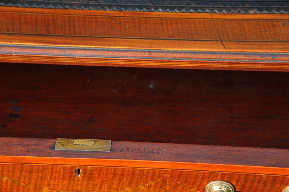 An antique Edwardian inlaid mahogany writing desk featuring a dark leather inset top, seven drawers with brass handles, and floral marquetry side panels. View XV
