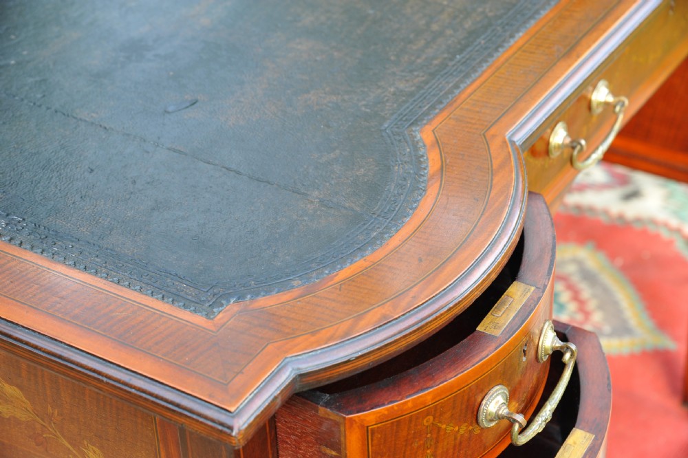 An antique Edwardian inlaid mahogany writing desk featuring a dark leather inset top, seven drawers with brass handles, and floral marquetry side panels. View XVI