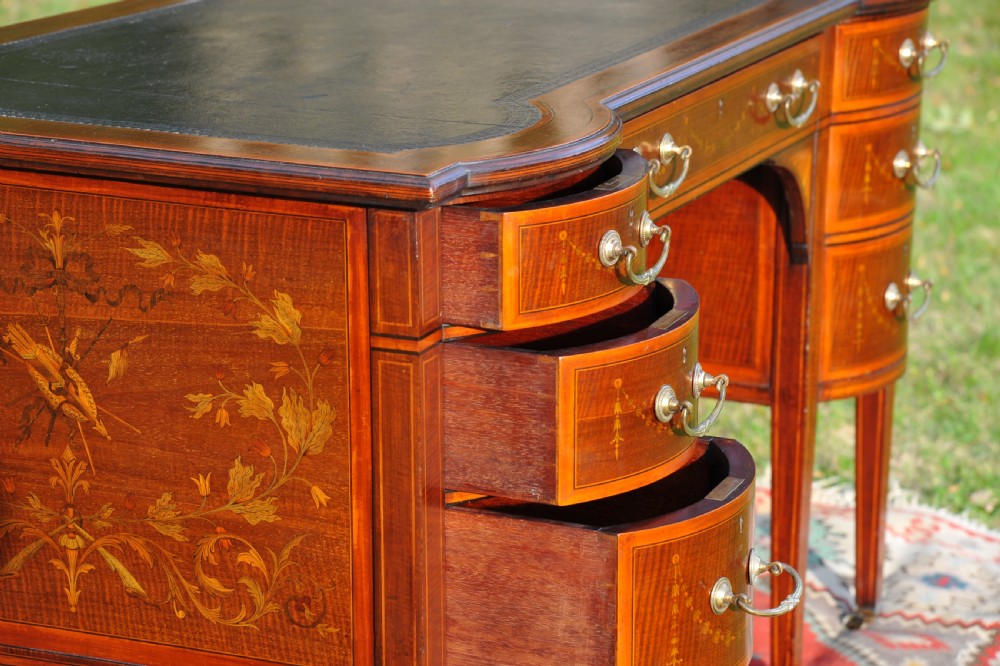 An antique Edwardian inlaid mahogany writing desk featuring a dark leather inset top, seven drawers with brass handles, and floral marquetry side panels. View XVII