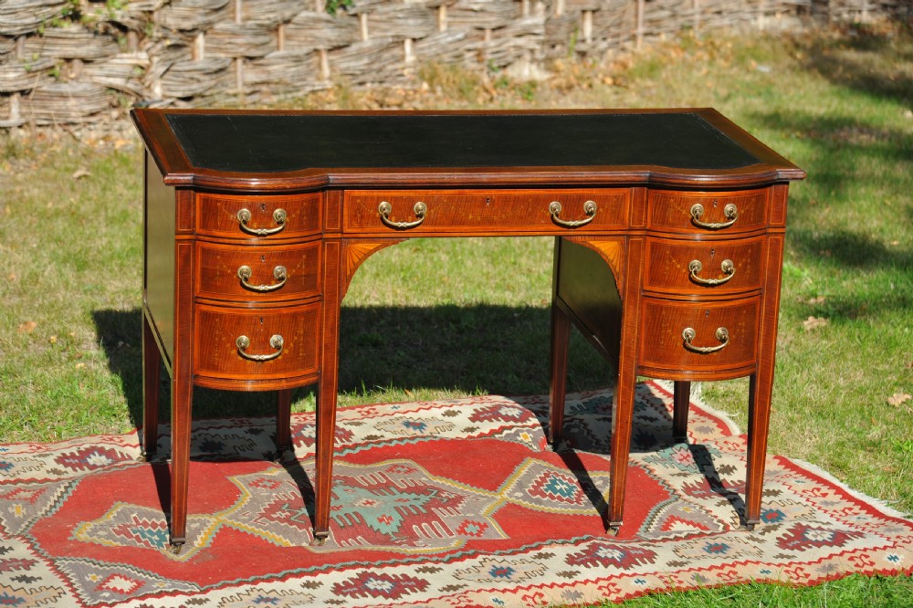 An antique Edwardian inlaid mahogany writing desk featuring a dark leather inset top, seven drawers with brass handles, and floral marquetry side panels. View XVIII