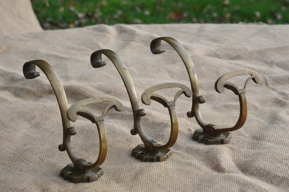 A set of three antique French cast bronze wall-mounted hat and coat hooks with scrolled upper arms and shaped lower pegs.