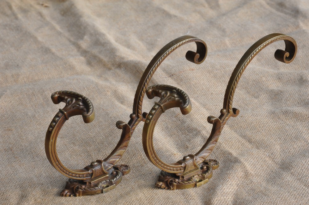 A pair of ornate antique French cast bronze dual-prong wall hooks featuring scrolling upper arms and decorative detailed bases.