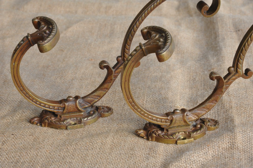 A pair of ornate antique French cast bronze dual-prong wall hooks featuring scrolling upper arms and decorative detailed bases. View V