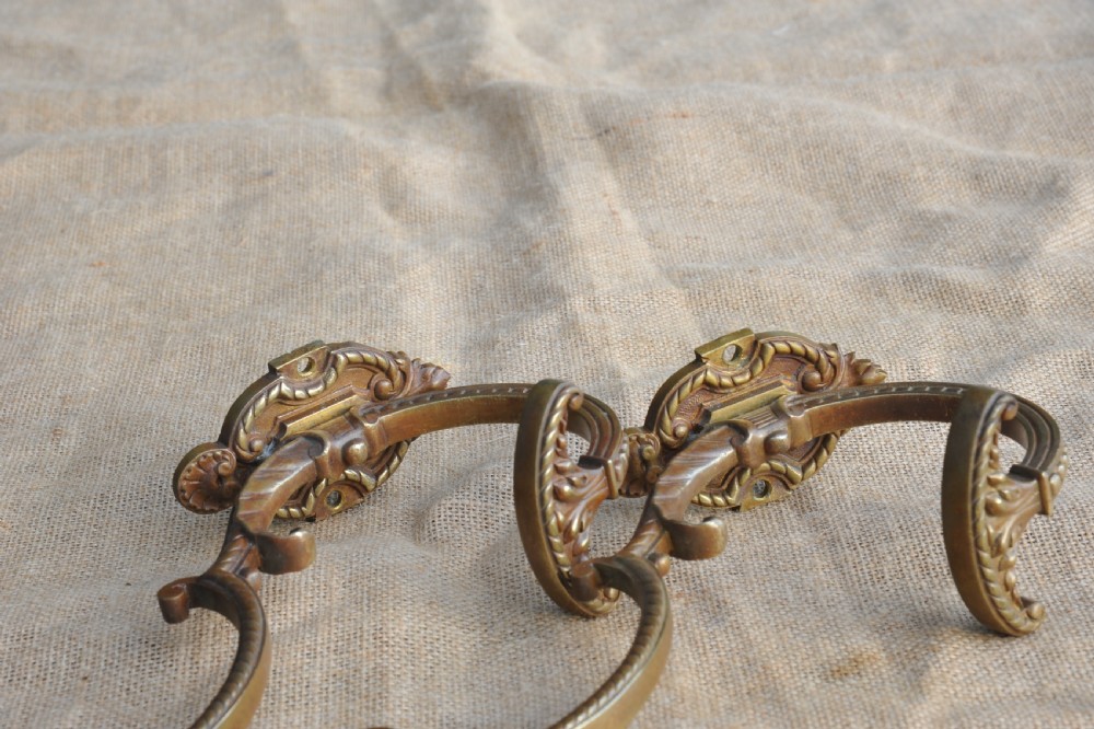 A pair of ornate antique French cast bronze dual-prong wall hooks featuring scrolling upper arms and decorative detailed bases. View VIII