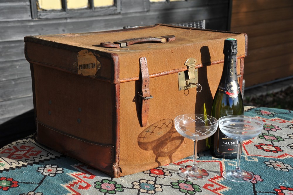A square antique tan canvas travel case featuring stitched brown leather edging, a top carrying handle, brass rivets, and an authentic Paddington railway paper label. View IX