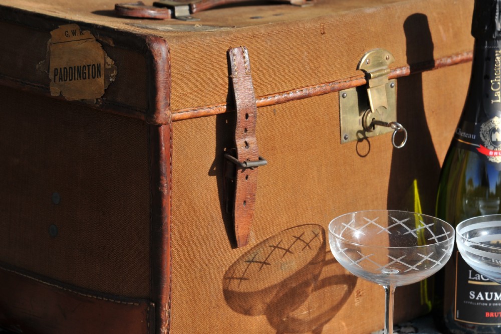 A square antique tan canvas travel case featuring stitched brown leather edging, a top carrying handle, brass rivets, and an authentic Paddington railway paper label. View II