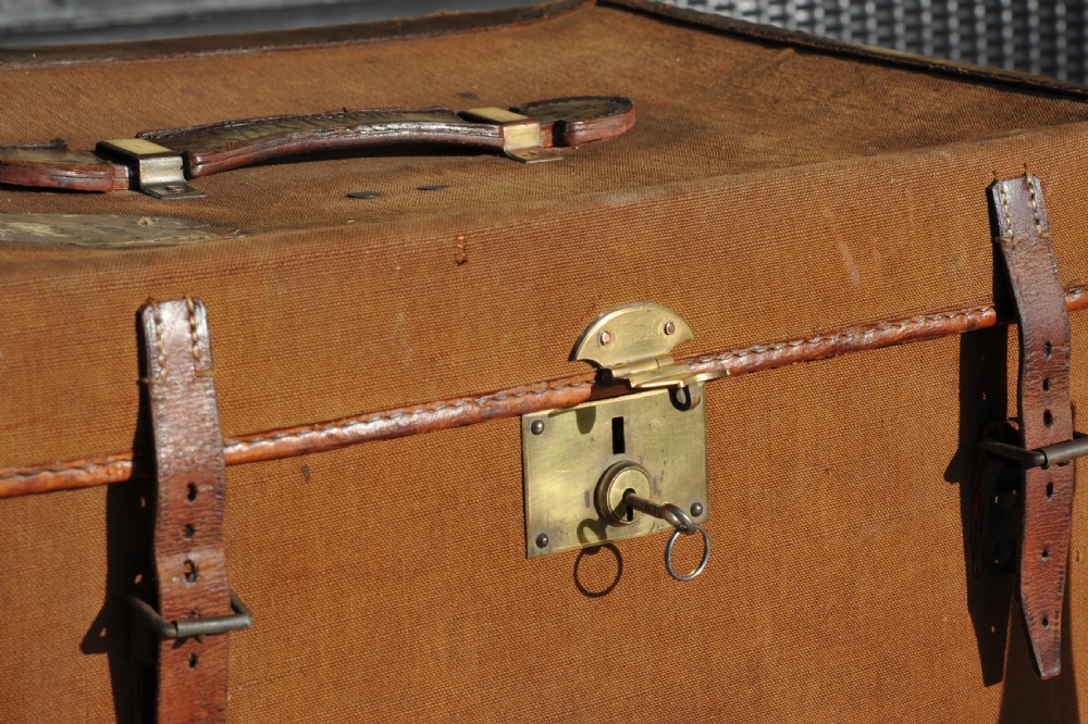 A square antique tan canvas travel case featuring stitched brown leather edging, a top carrying handle, brass rivets, and an authentic Paddington railway paper label. View III