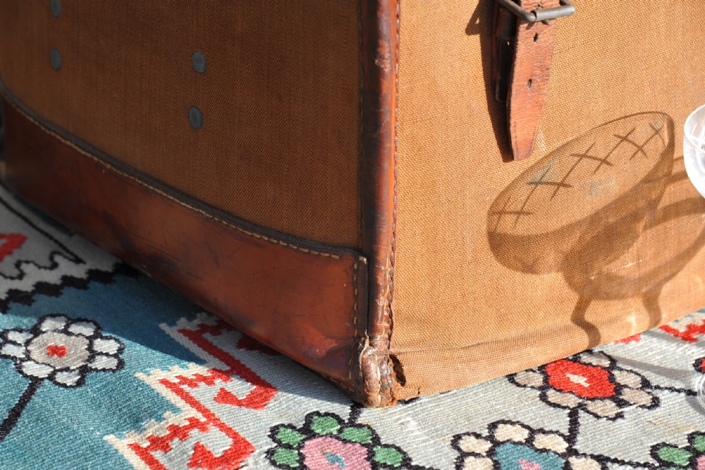 A square antique tan canvas travel case featuring stitched brown leather edging, a top carrying handle, brass rivets, and an authentic Paddington railway paper label. View VI