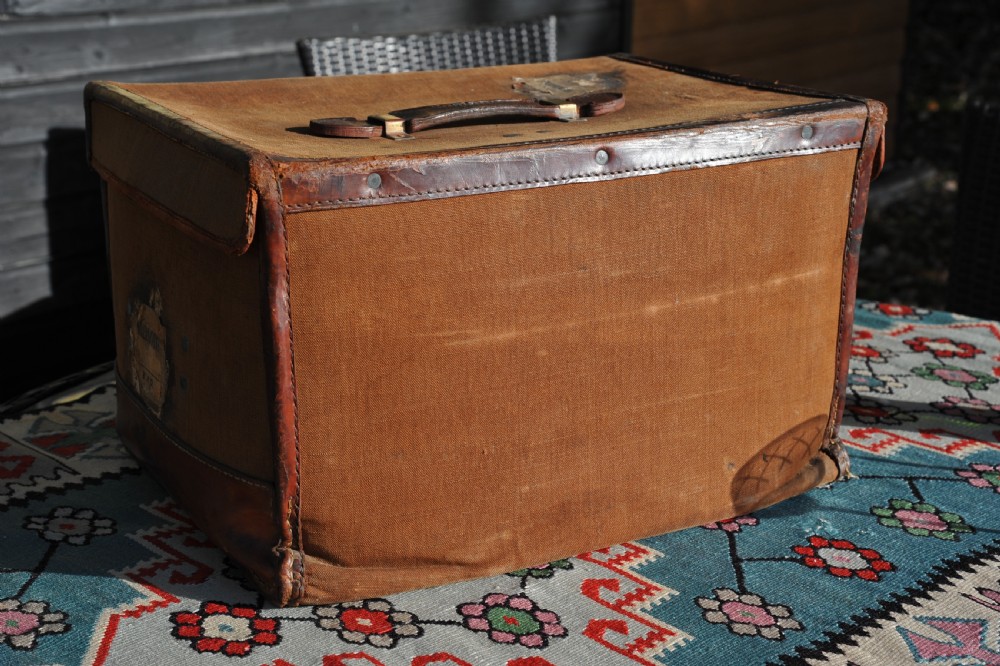 A square antique tan canvas travel case featuring stitched brown leather edging, a top carrying handle, brass rivets, and an authentic Paddington railway paper label. View VIII