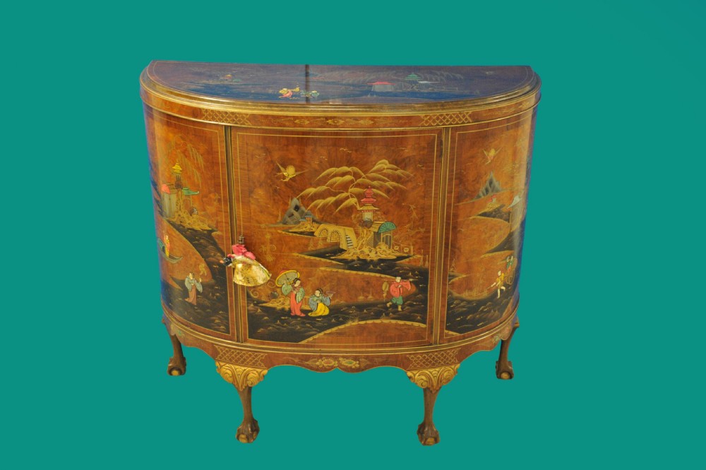 A circa 1910 semi-circular demi-lune cabinet featuring hand-painted Chinoiserie figures and landscapes with gilt details on cabriole legs.