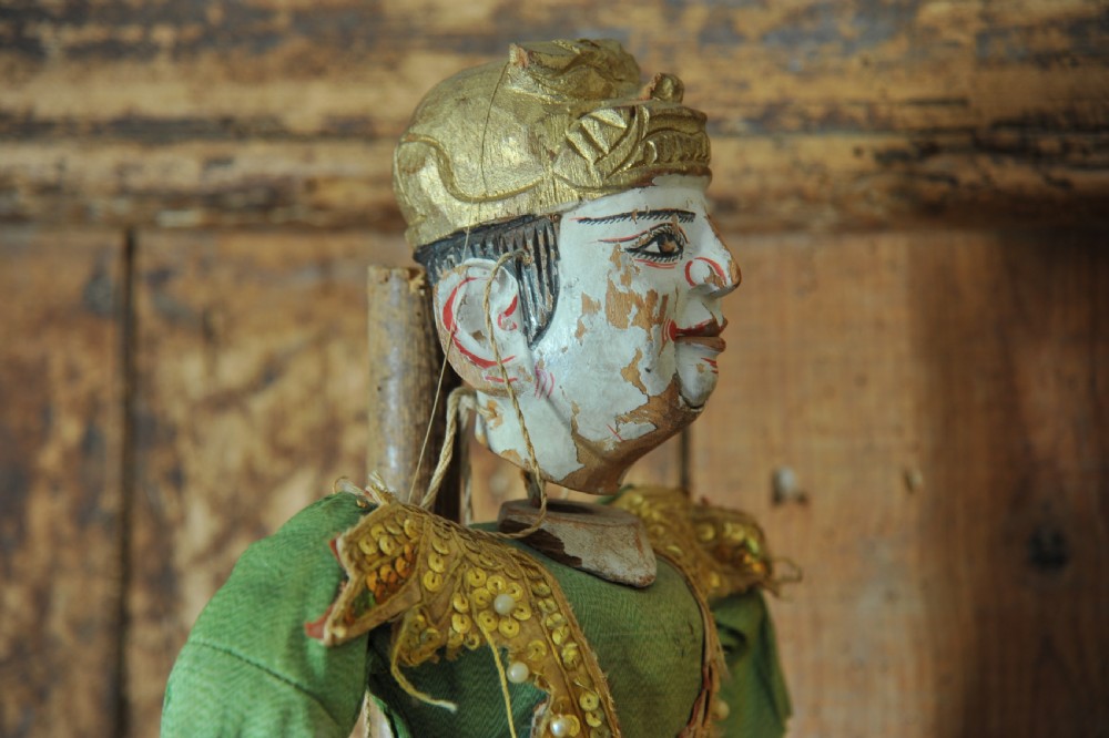 An antique carved wooden marionette puppet wearing a green top and embellished red and white skirt, mounted on a circular base. View II