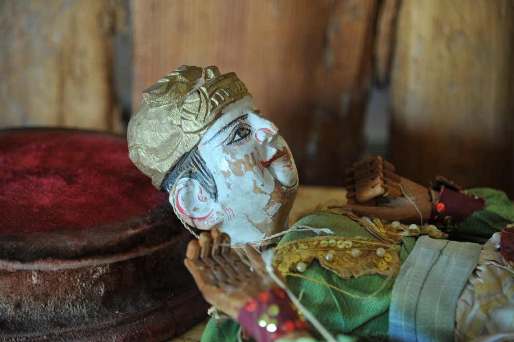 An antique carved wooden marionette puppet wearing a green top and embellished red and white skirt, mounted on a circular base. View VIII