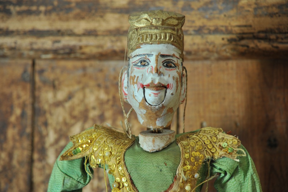 An antique carved wooden marionette puppet wearing a green top and embellished red and white skirt, mounted on a circular base. View XV