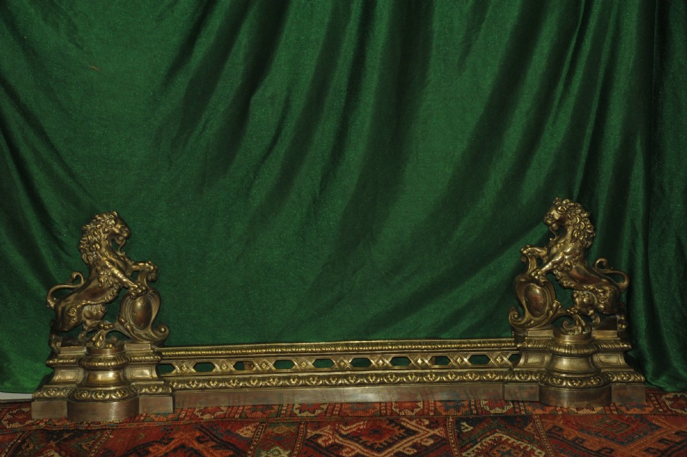 A cast brass Louis XV style fireplace fender featuring a central pierced lattice gallery flanked by two sculpted lions resting on shields.